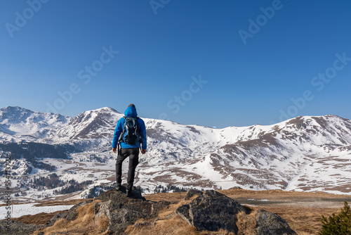 Rear view of man with backpack looking at snow capped mountain peak Zirbitzkogel and Kreiskogel in Seetal Alps, Styria (Steiermark), Austria, Europe. Hiking trail Central Alps in winter on sunny day