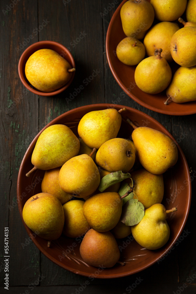 pears in clay plates on dark background in rustic style.