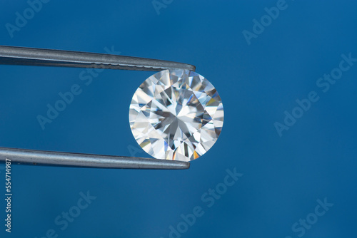Round diamond faceted cubic zirconia, cubic crystalline form of zirconium dioxide (ZrO2) colorless synthesized material. White synthetic gemstone. Diamond imitation. Blue background.