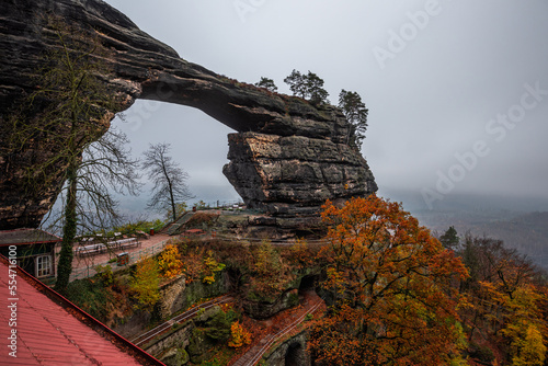 Hrensko, Czech Republic - The famous Pravcice Brana (Pravcicka Gate) in Bohemian Switzerland National Park, the biggest natural arch in Europe on a foggy day with colorful autumn foliage photo