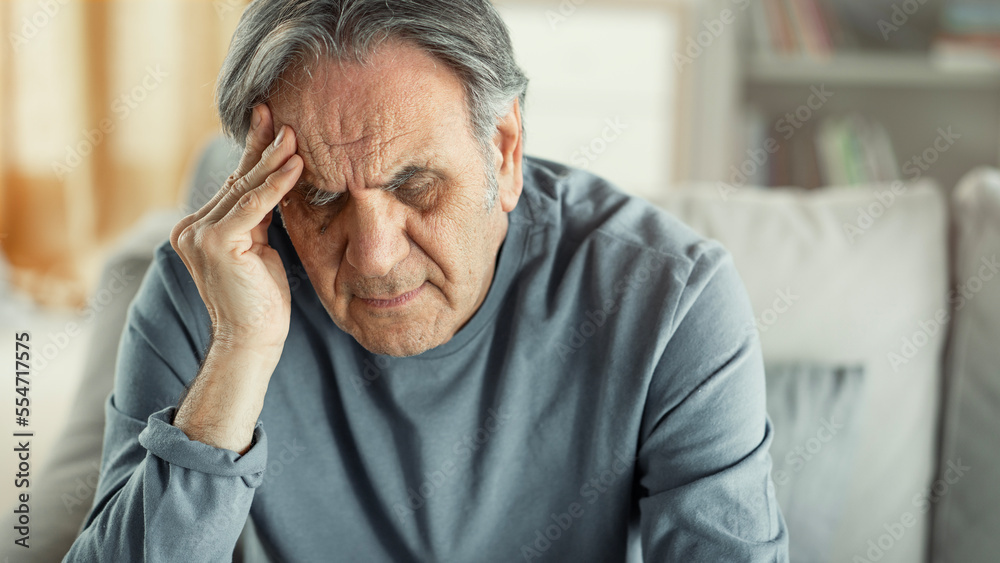 Old man holding his forehead sitting alone at home Old man holding his forehead sitting alone at home