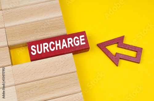 On a yellow surface are wooden blocks and an arrow pointing to a block with the inscription - Surcharge