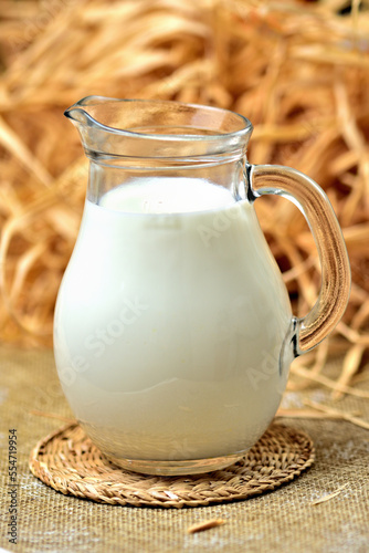 Healthy fresh cow milk in a transparent glass jug. Dry straw and hay as decoration in the background. Close-up. Vertical photo.