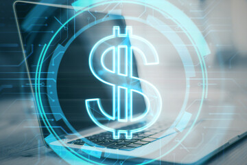 Close up of desktop with laptop and glowing dollar sign on blurry background. Money and online banking concept. Double exposure.