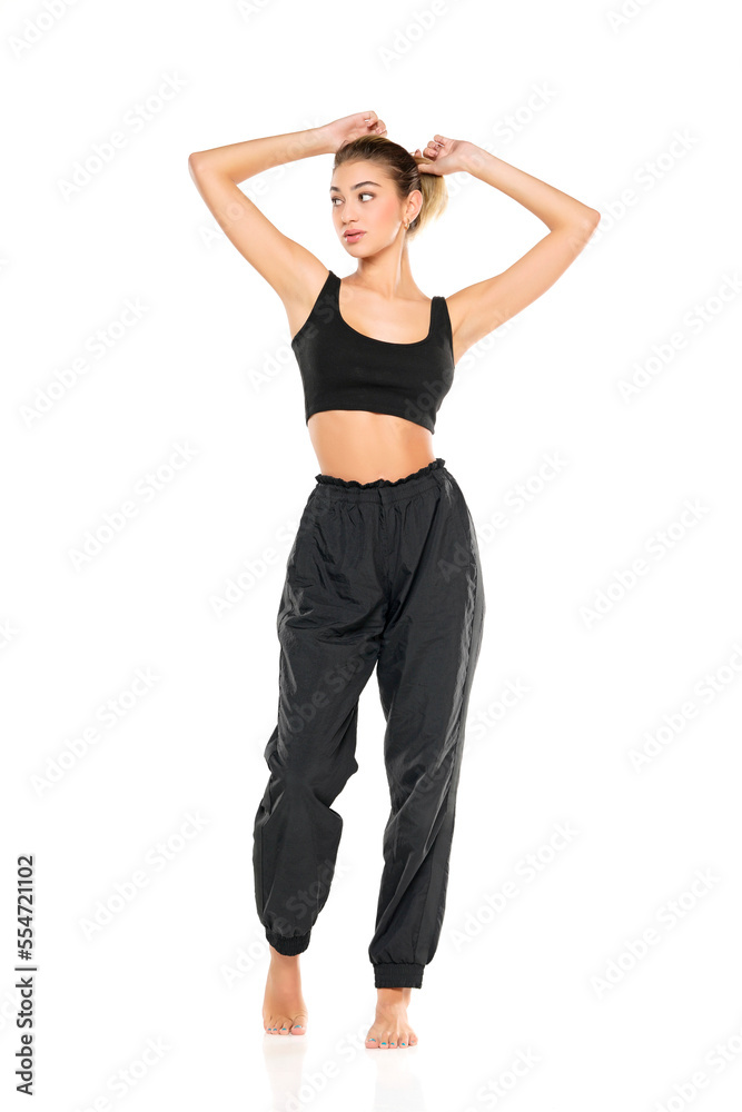 a young barefeet woman in black sweatpants and a tank top on a white background