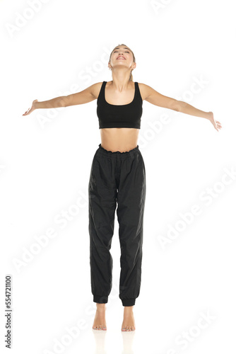 a young barefeet happy woman in black sweatpants and a tank top on a white background