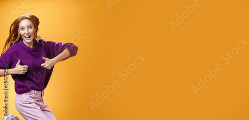 Excited and happy funny young redhead female in purple sweater jumping from happiness and satisfacion showing thumbs up gesture in approval giving positive reply and liking awesome clothes photo