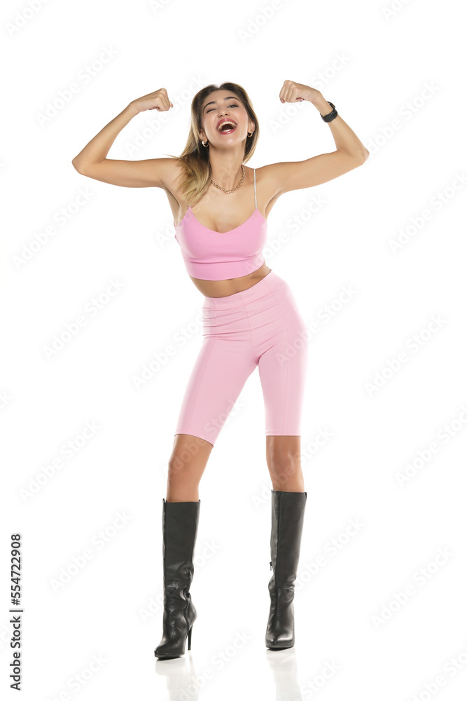 a young happy woman in pink short leggings and top, and black leather boots on a white background a young happy woman in pink short leggings and top, and black leather boots on a white background