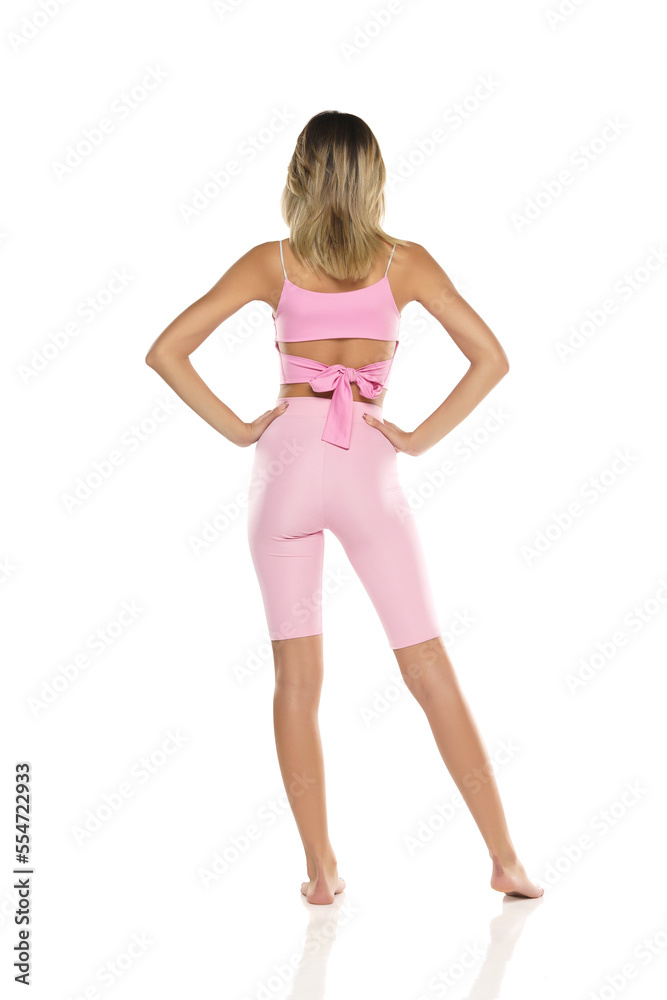 a young barefeet woman in pink short leggings and top posing on a white background. Back, Rear View