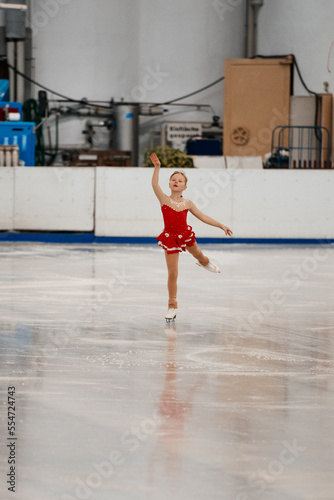 a little girl in a red dress participates in a figure skating competition