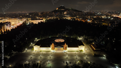 Aerial drone night shot of renovated public neoclassic building of Zappeion used for events and meetings in the National Gardens of Athens and Lycabettus hill aligned at the background, Greece photo