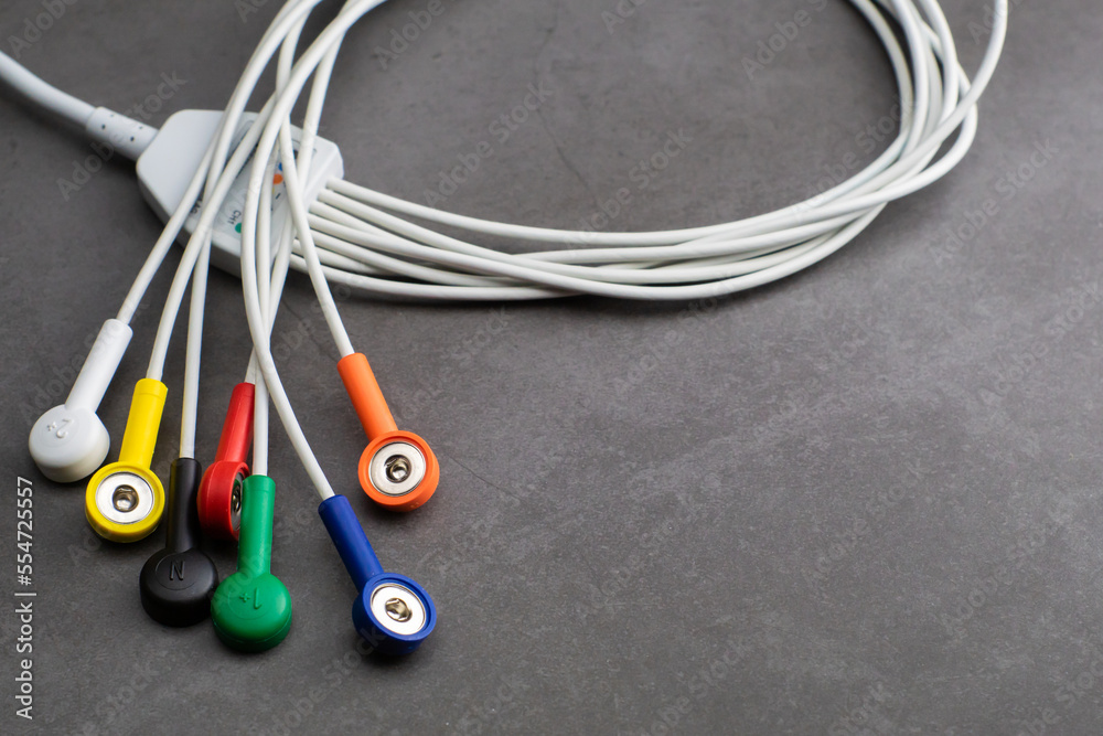 Colored wires and cables of Holter monitor device measuring heart rate and blood pressure with a copy space below on gray background.