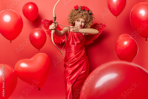 Foto Serious woman in role of cupid shoots arrow wears elegant dress tries to find lo