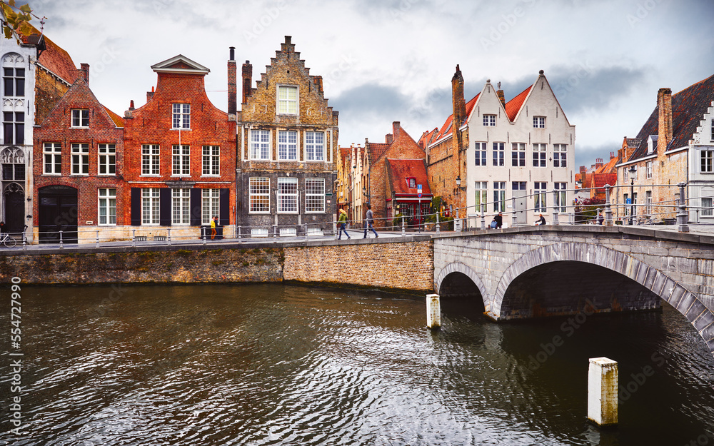 Bruges Belgium vintage stone houses and bridge over canal ancient medieval street picturesque landscape in summery sunny day with blue sky white clouds