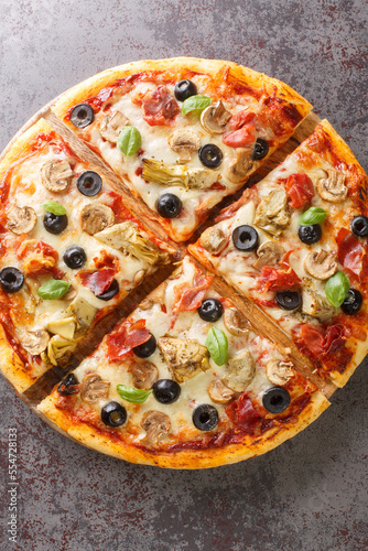 Italian cuisine Pizza capricciosa prepared with mozzarella cheese, ham, mushroom, artichoke, tomato and olive closeup on the wooden board on the table. Vertical top view from above