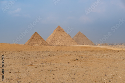 The three great pyramids of Giza seen from a side angle, blue sky with some haze.