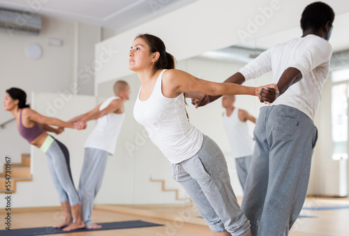 Young women maintaining healthy lifestyle practicing yoga with partner at group lesson