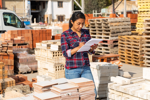 Female worker with tablet checking quantity of paving slabs in warehouse of building materials