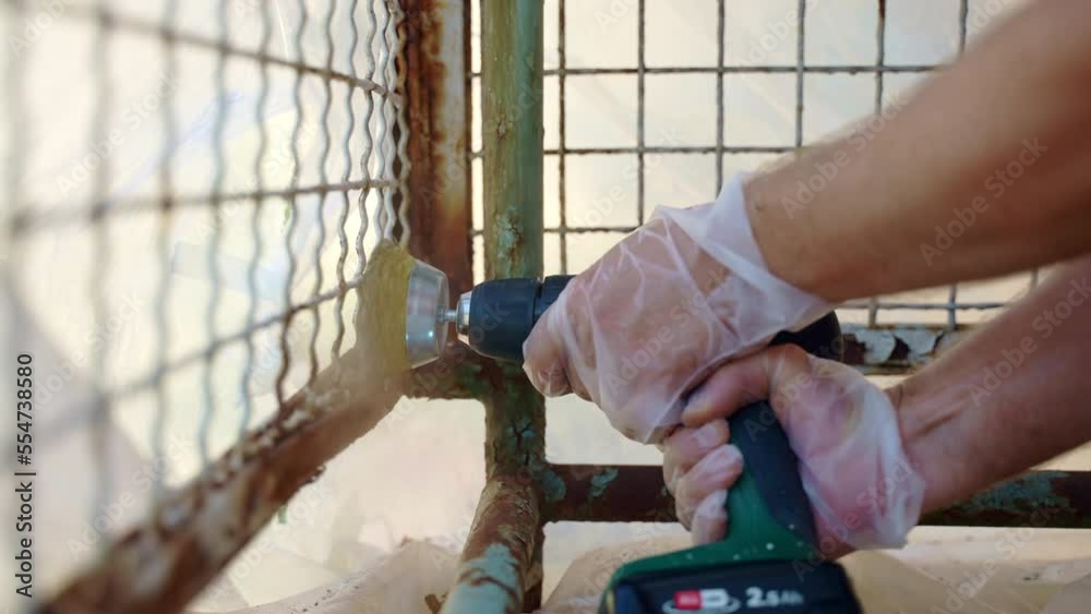 Workman using electrical grinder with metal brush nozzle for removing