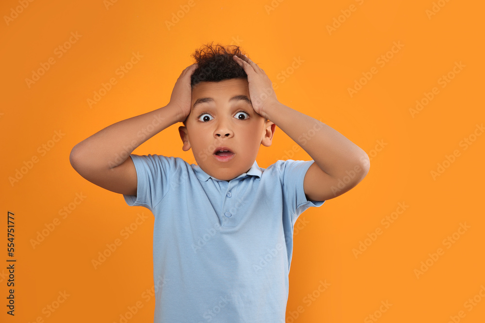 Portrait of emotional African-American boy on orange background