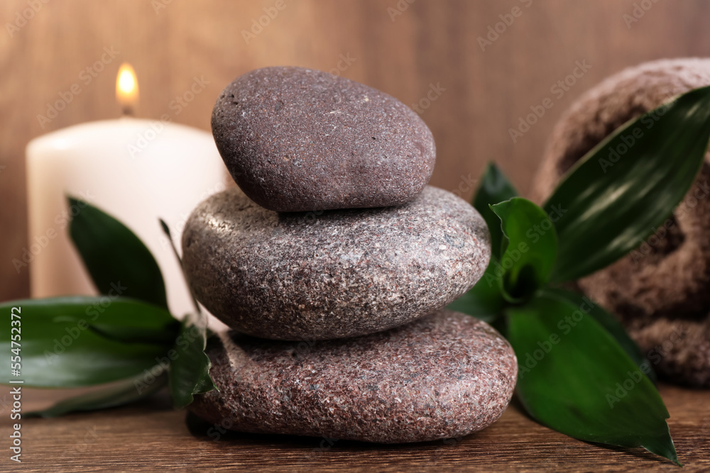 Stacked spa stones, bamboo leaves, candle and towel on wooden table, closeup Stacked spa stones, bamboo leaves, candle and towel on wooden table, closeup