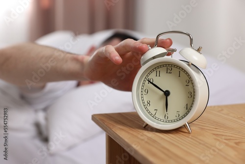 Man turning off alarm clock in bedroom, focus on hand