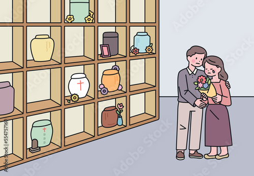 A man and a woman mourn with flowers in a memorial house with a cremation urn.