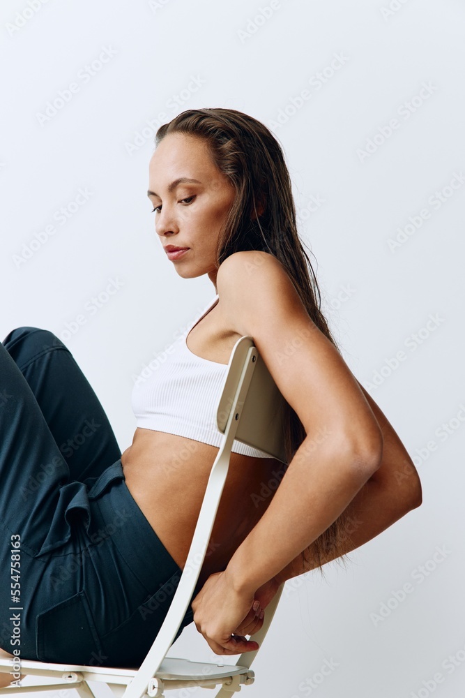 A woman sits on a chair with a beautiful skin tan on a white background in the room A woman sits on a chair with a beautiful skin tan on a white background in the room