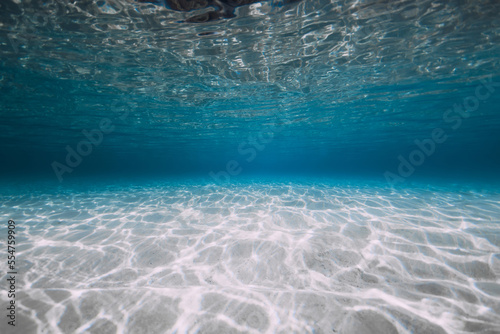 Blue ocean with white sand and sunlight underwater. Transparent ocean background