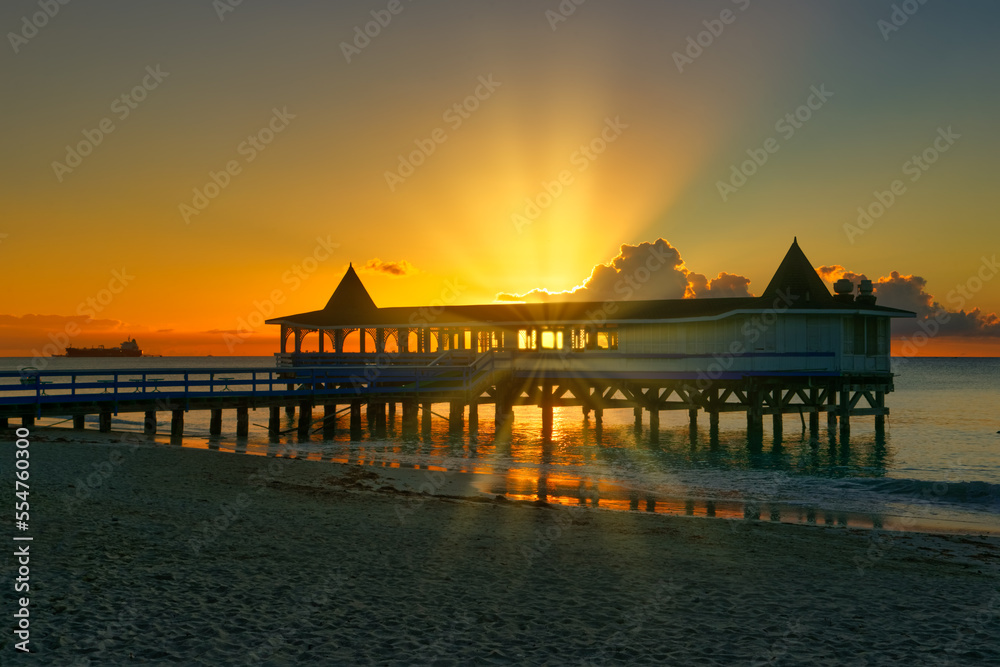 Beautiful Caribbean sunset with sunburst, setting behind a building by the ocean, copy space