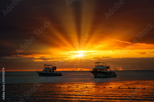 Beautiful sunset over sea with sunburst reflection and silhouettes of two small boats