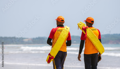 Two Lifeguards on duty at the tropical beach, Both carrying rescue tubes on their shoulders and walking in Weligama, Sri Lanka.