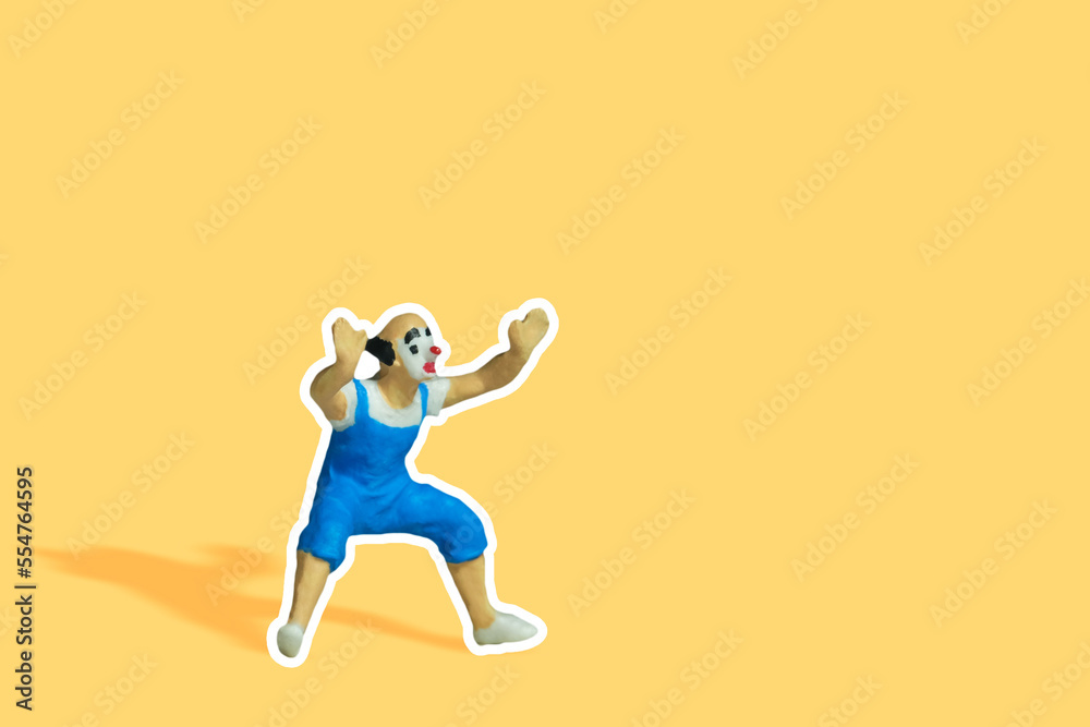 Miniature people toy figure photography. Side front view of bald clown wearing blue dress in sticker style on yellow pastel background