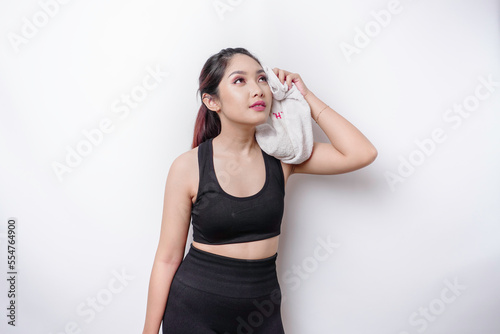 Sportive Asian woman posing with a towel on her shoulder, tired after workout