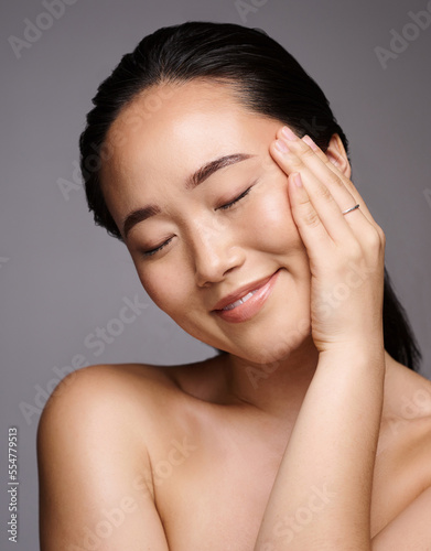 Face, beauty and skincare with a model asian woman touching her skin in studio on a gray background. Relax, wellness or cosmetics with an attractive young female posing for a luxury skin care product