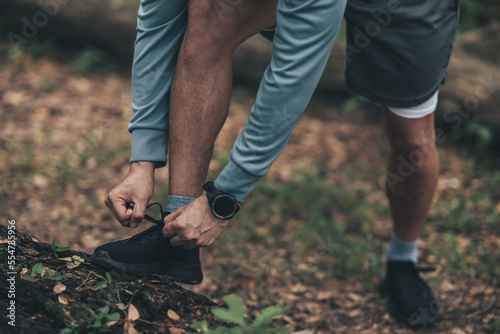 Sport man  tying jogging shoes in the forest. Outdoor workout   Healthy lifestyle concept.