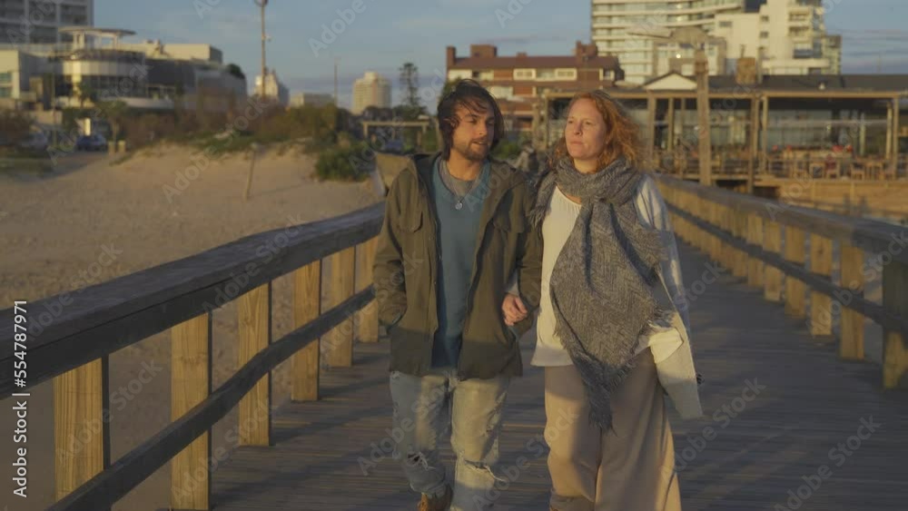 Pregnant couple holding hands walking by pier at sunset. Pregnant couple holding hands walking by pier at sunset.