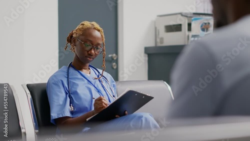 Medical assistant analyzing checkup reports in waiting lobby, sitting in hospital reception area. Professional worker looking at registration papers before treating patient in clinic. Handheld shot. photo