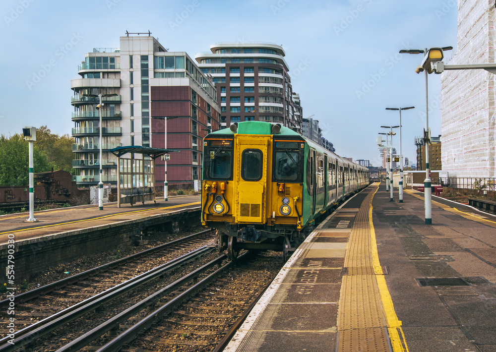 British passenger train arriving at platform; railroad tracks and platform in foreground; residential buildings in background