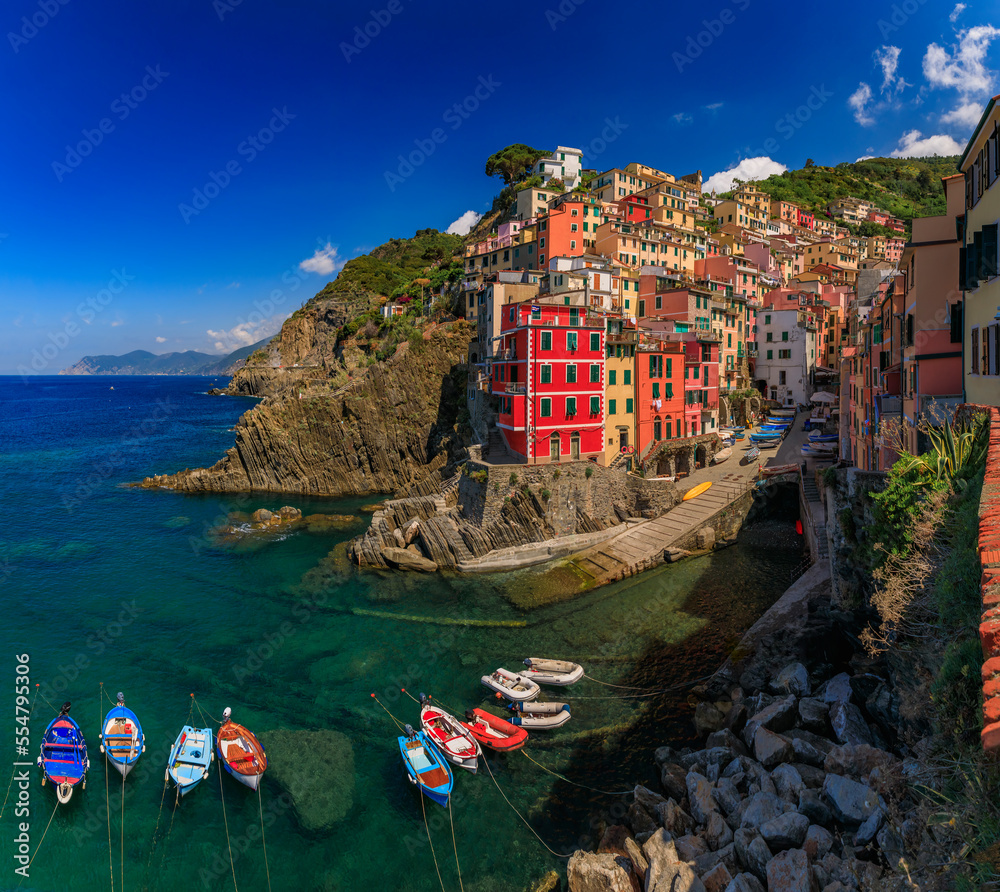 Daytime view onto the Mediterranean Sea with traditional boats and colorful houses in old town of Riomaggiore in Cinque Terre, Italy on a sunny day