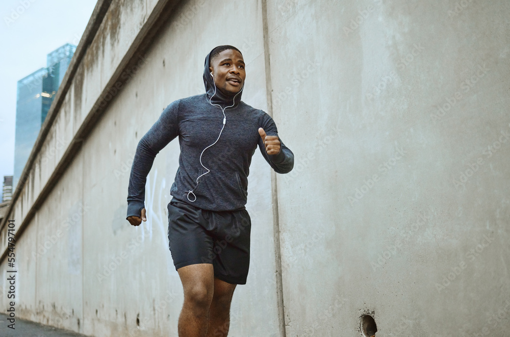 Black man, fitness and running in the city with earphones listening to music during cardio workout. Active African American man runner enjoying audio track, healthy exercise or training in urban town - obrazy, fototapety, plakaty 