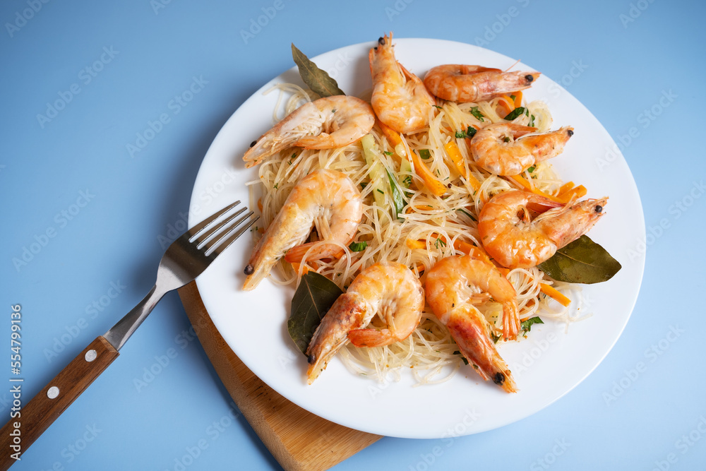 Funchosa is a dish of Korean cuisine with shrimp on a white plate and on a blue background with a fork. Funchosa is a dish of Korean cuisine with shrimp on a white plate and on a blue background with a fork.