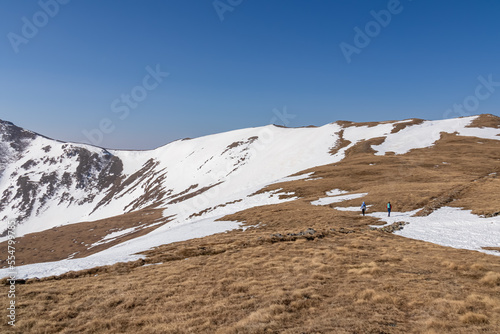 Two people on panoramic hiking trail from Hohe Ranach to Zirbitzkogel and Kreiskogel, Seetal Alps, Styria (Steiermark), Austria, Europe. Snow covered idyllic mountain ridges on sunny early spring day photo