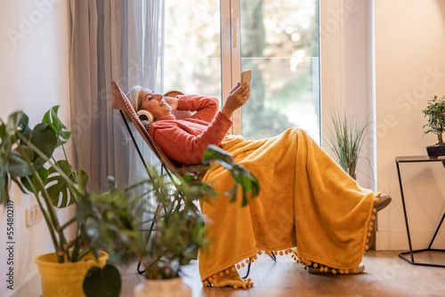 Φωτογραφία Senior woman at home listening to music with smart phone and headphones,senior w