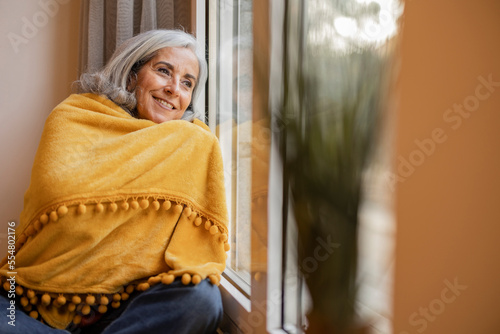 elderly woman with blanket at home looks out the window, a cold day photo