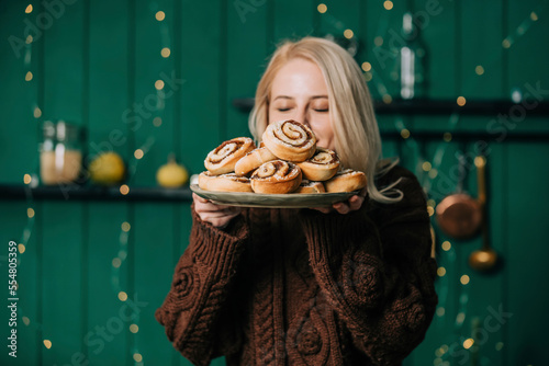 Woman with eyes closed smelling cinnamon buns on plate at home photo