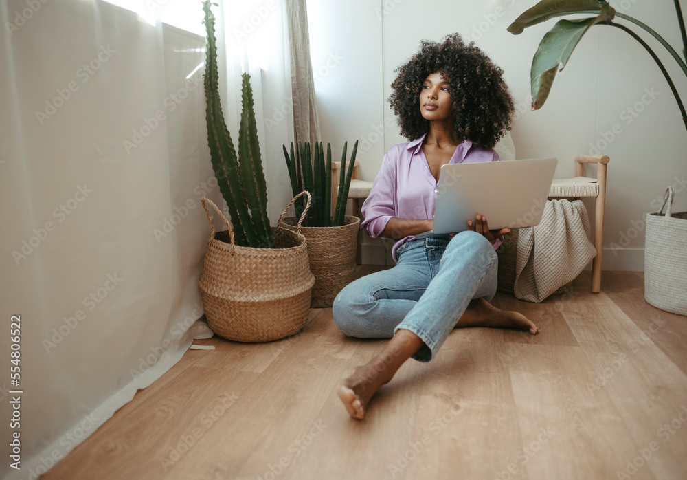 Contemplative woman with laptop sitting on floor at home