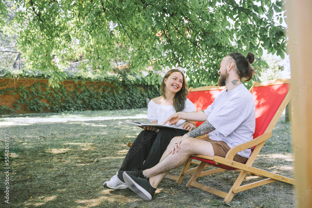 Happy couple with book sitting on deck chairs in backyard