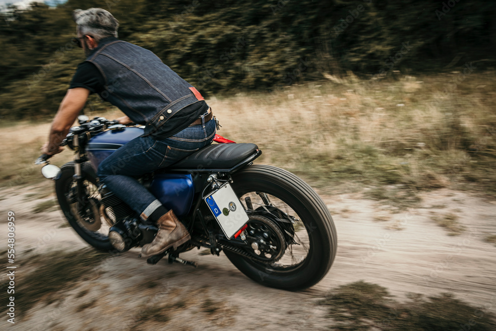 Mature biker riding motorcycle on dirt road Mature biker riding motorcycle on dirt road