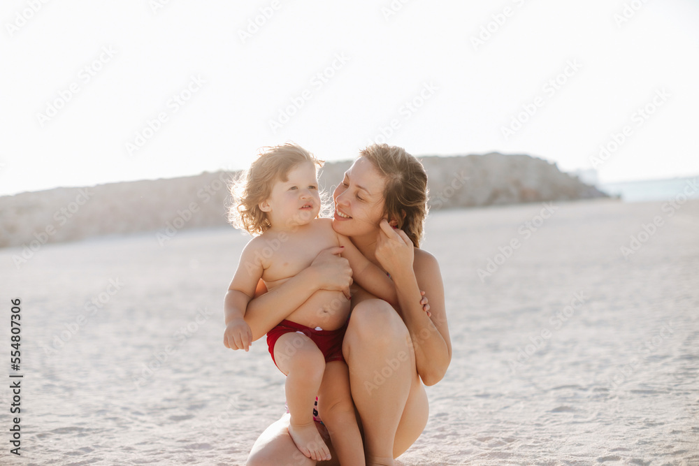 Smiling mother embracing son kneeling at beach enjoying vacation Smiling mother embracing son kneeling at beach enjoying vacation
